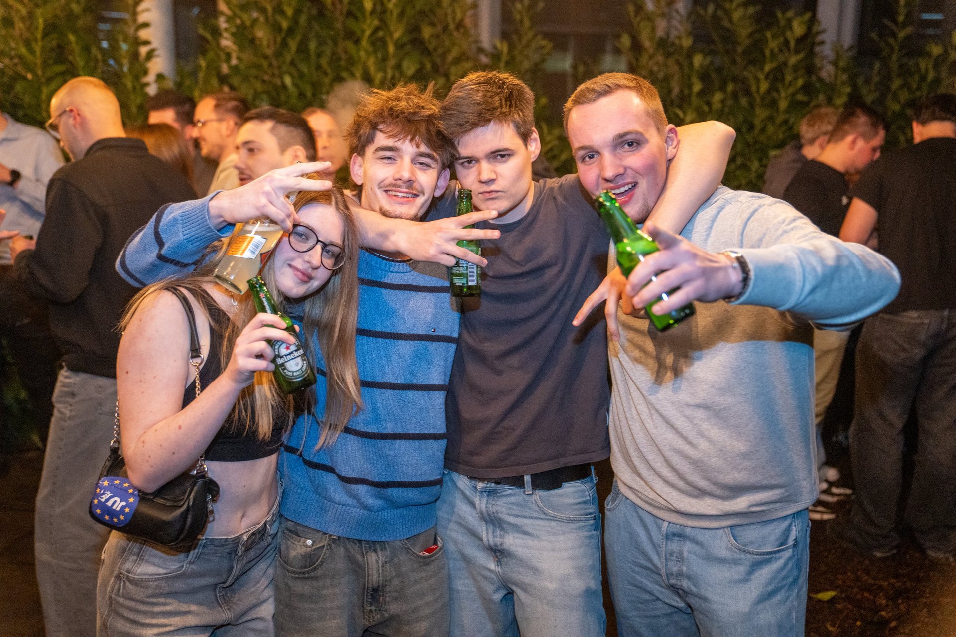 Four young people posing together at a social gathering, smiling and holding drinks