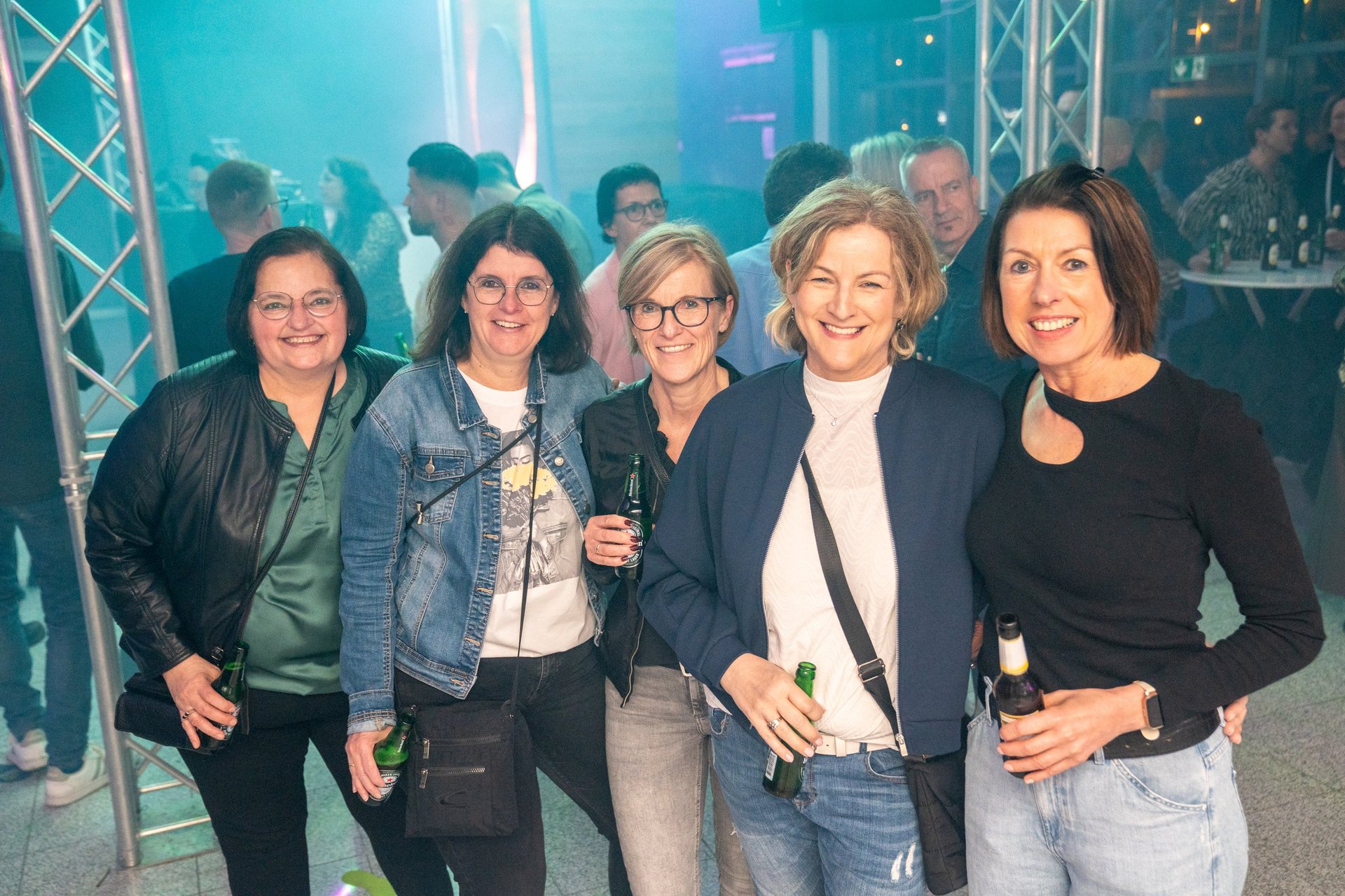 Five women smiling at camera at an indoor event with blue lighting and event structures in background
