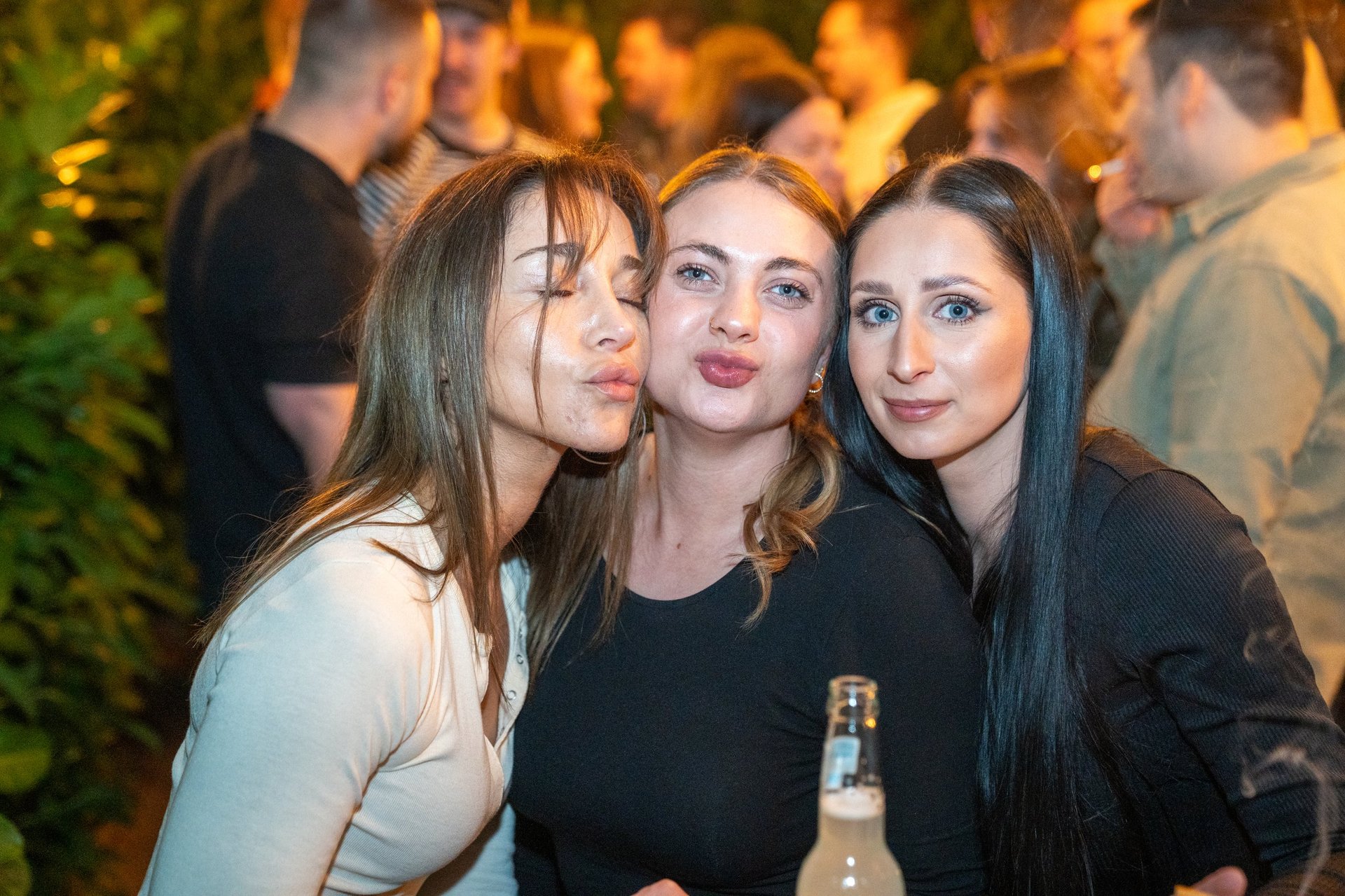 Three women smiling at camera at indoor party with warm lighting and fireplace in background